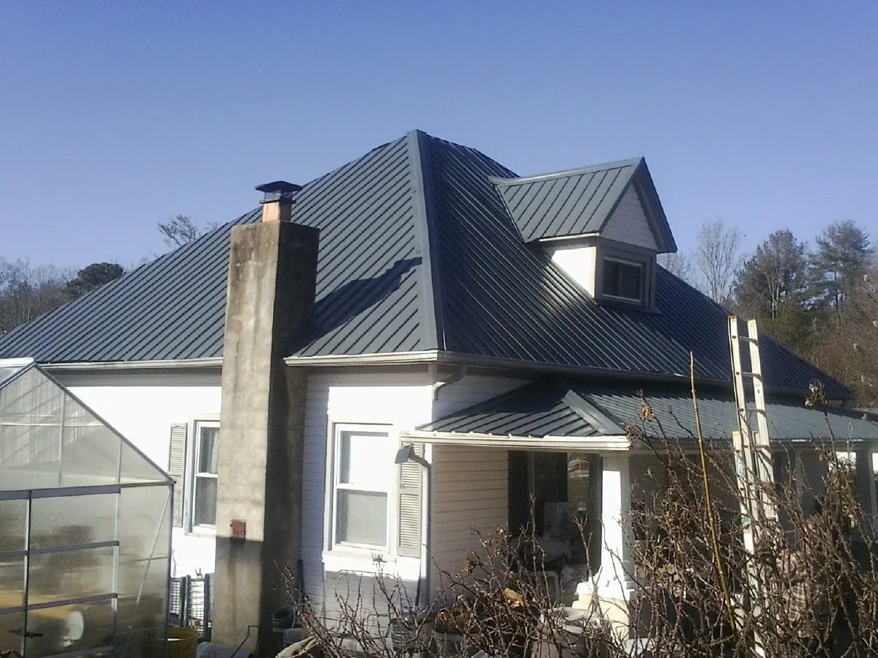 Dark blue standing seam metal roof on a white farmhouse with dormer — Slate & Tile Roof Repair by Roofing Brothers in Bel Alton