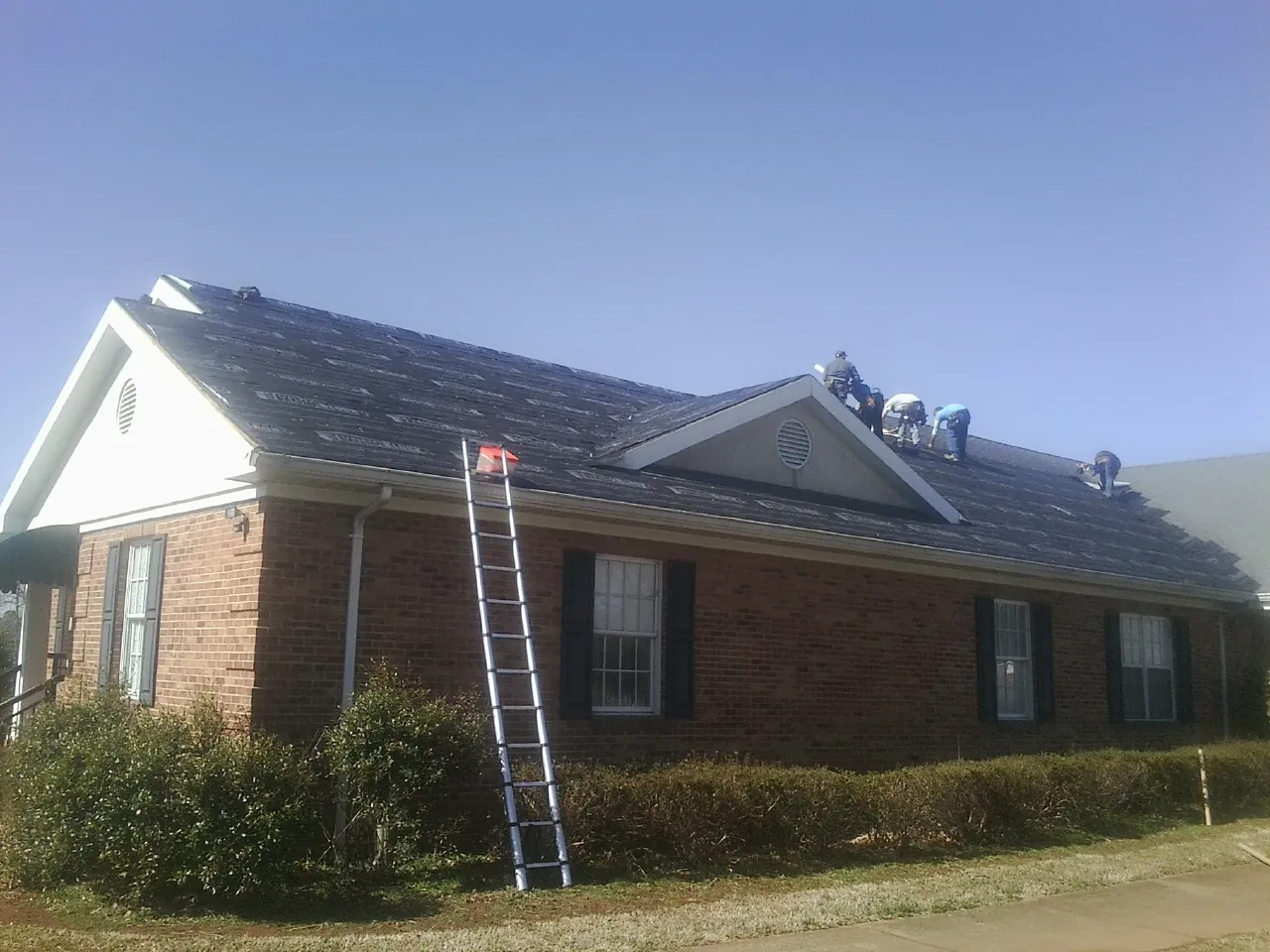 Crew tearing shingles off a brick ranch roof with a ladder set — Emergency Roof Repair work by our crew in Bel Alton
