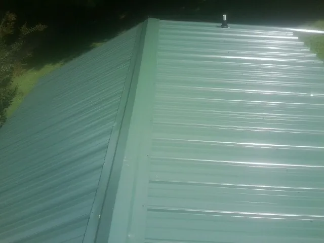 New green metal panels meeting at the ridge of a roof — Flat Roof Repair work by our crew in Bel Alton