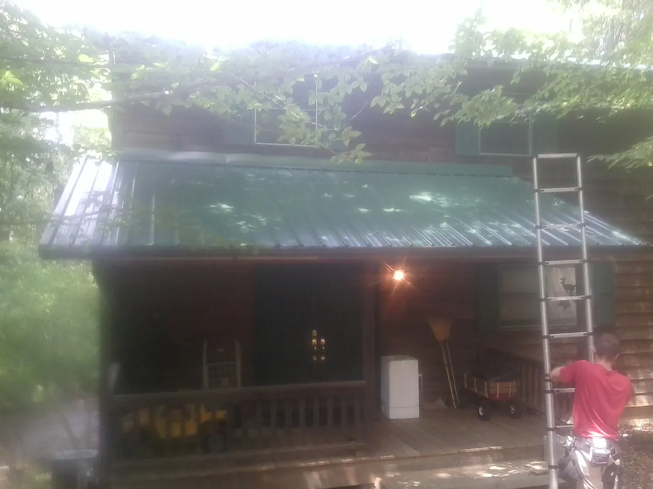 Worker on a ladder at the green porch roof of a wooded cabin in Bel Alton