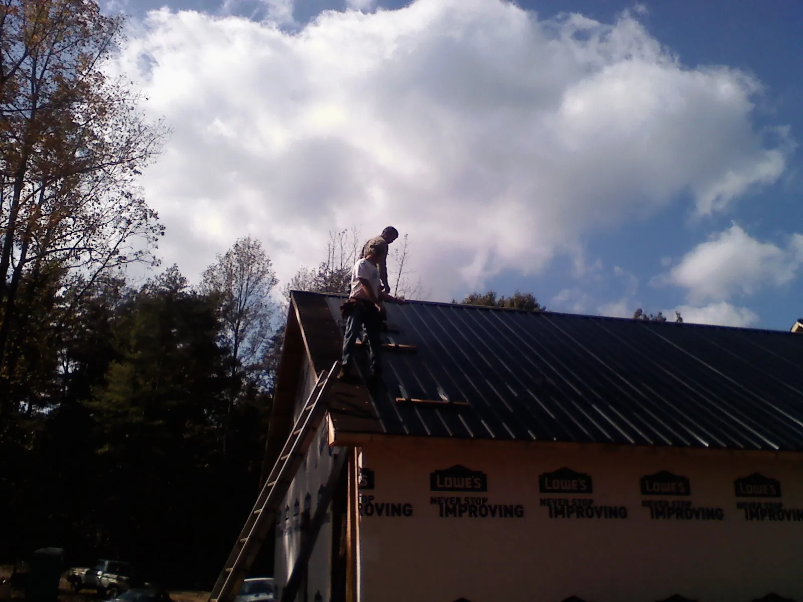 Roofer fastening dark metal panels high against a cloudy sky, from a Roof Inspection job in Bel Alton
