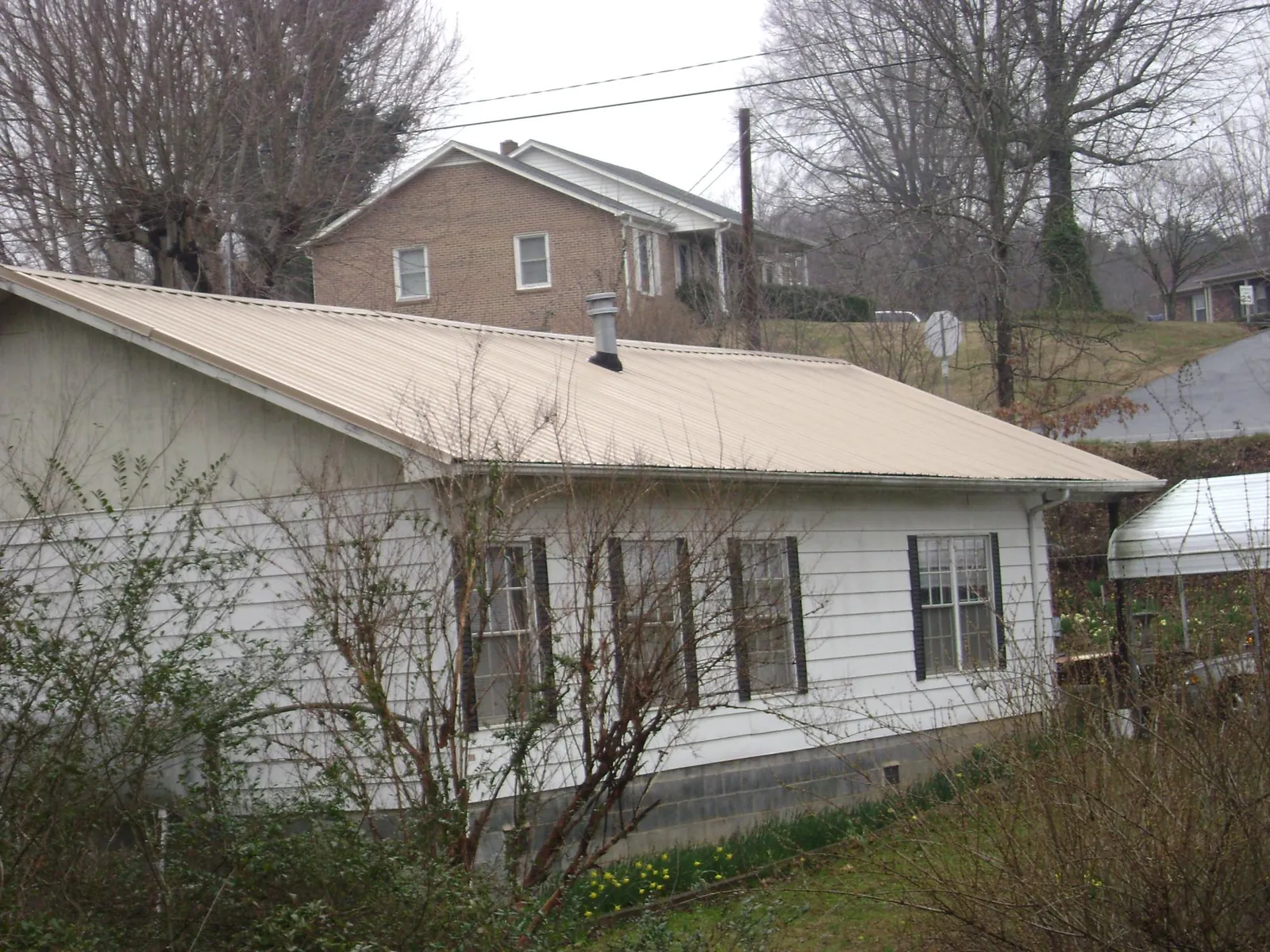Tan metal roof on a white sided house set into a hillside — Commercial Roofing by Roofing Brothers in Bel Alton